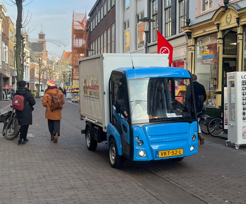 Kleine blauwe elektrische vrachtauto rijdt door de winkelstraat